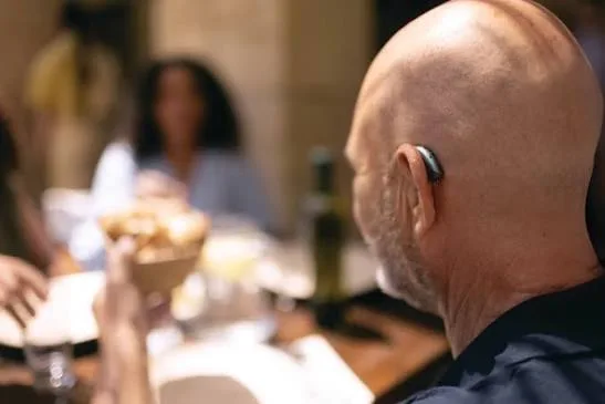 A man wearing a hearing aid following conversation at a busy restaurant table
