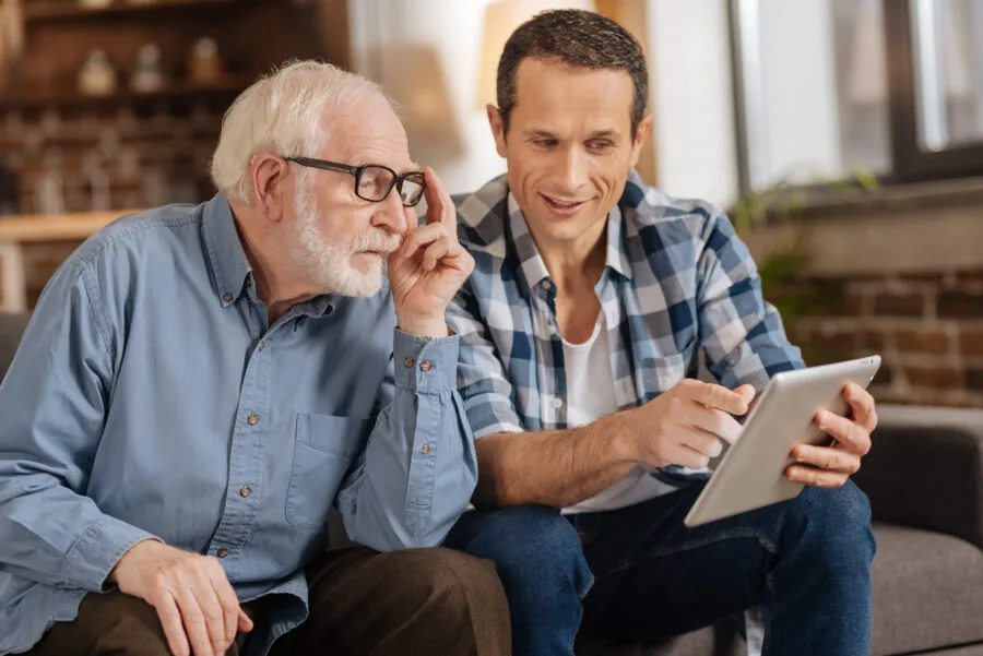 An older man and a younger man looking at hearing aid options together on a tablet