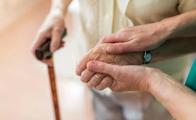 A carer holding the hands of an older person using a walking stick